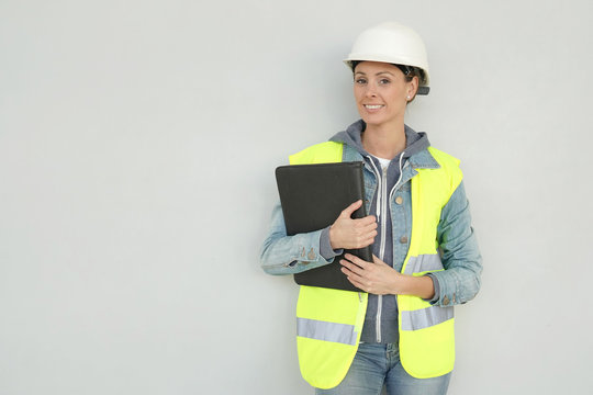 Smiling Female Construction Worker In Safety Gear On Grey Background