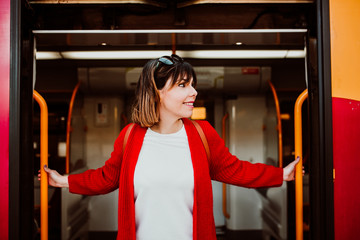 .Young woman with short hair and red jacket excited with her travel around europe. Ride on a train at the train station of oporto, portugal. Lifestyle