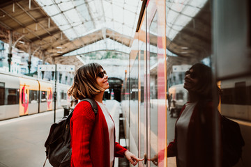 .Young woman with short hair and red jacket excited with her travel around europe. About to take a train at the train station of oporto, portugal. Lifestyle