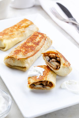 Crepes with chicken and mushrooms close-up on a table and sour cream. Top view, space for text.