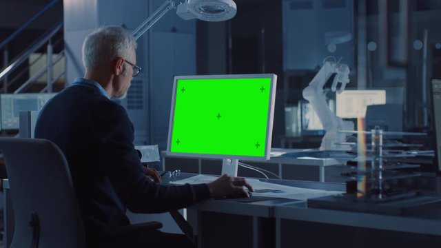 Professional Heavy Industry Engineer Works on Green Mock-up Screen Computer. Engineering Bureau and Industrial Design Agency with Various Robotic, Architectural and Machinery Components