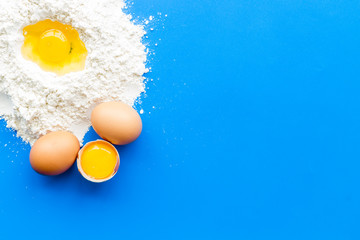 Making dough concept. Pile of flour and eggs on blue background top view copy space