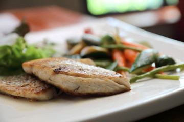 Sea bass fillet with grilled vegetables and salad on wooden table