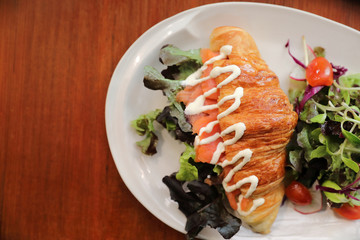 Croissant bread with salmon and salad on wooden background