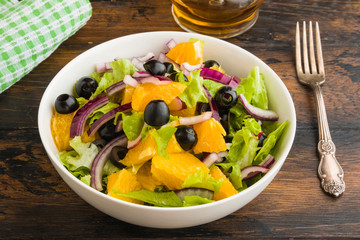 Healthy vegetarian salad with oranges, lettuce, black olives and red onion in white bowl on wooden rustic table