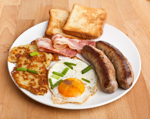 plate with classic fried egg, hash browns and bacon breakfast on a wooden table