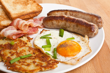 plate with classic fried egg, hash browns and bacon breakfast on a wooden table