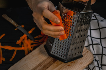 Male hands grate carrot on a grater. Chef cooking. Shredding vegetables.