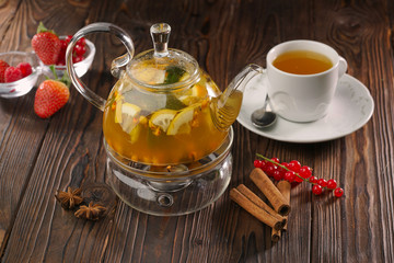 Fruit tea in glass teapot and white cup on wooden background with fresh berries