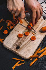 Cutting carrot into circles on a wooden board. Cooking process.