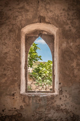 Fototapeta na wymiar View at some grean leaves and blue skies through an open window with plastered walls from an old abandoned medieval building in Kato Chora, Kythira, Greece