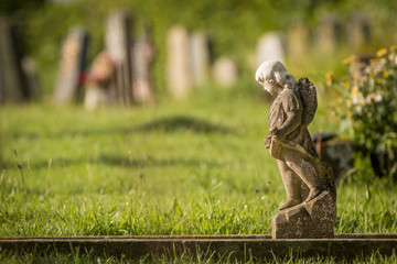 Small stone statue of an angel on a grave on a graveyard in Scotland with a blurry background of tombstones