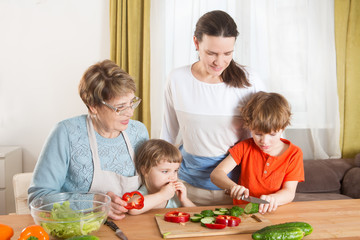 Happy family mother, grandma and two little kids are preparing the vegetables in salad in the kitchen. Healthy Lifestyle food.