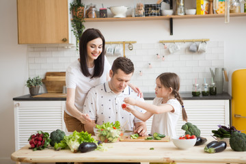 Happy family Mother. father and daughter in preparing healthy vegetables  together  in the kitchen. Help children to parents. 