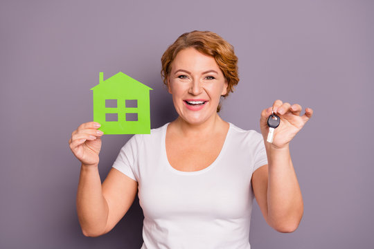 Portrait of her she nice lovely charming attractive cheerful cheery positive wavy-haired lady in casual white t-shirt holding in hand showing key green home isolated over gray violet purple background