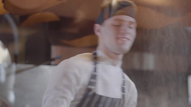 Slow motion of handsome pizza maker spinning and tossing pizza dough up