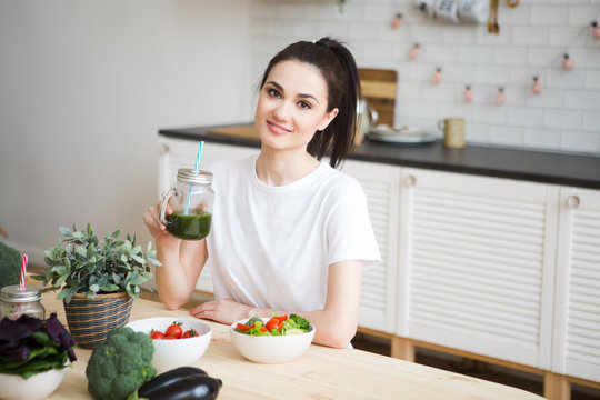 Smiling young woman drinking green smoothie juice in kitchen. Healthy Lifestyle.