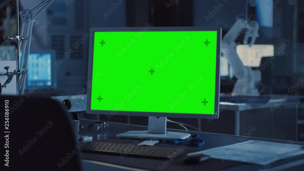 Leinwandbilder  On the Desk Computer with Isolated Green Mock-up Screen Display. In the Background Robot Arm Concept Standing in Heavy the Dark.Industry Engineering Facility