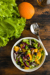 Healthy vegetarian salad with oranges, lettuce, black olives and red onion in white bowl on wooden rustic table, top view