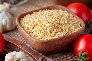 Uncooked raw bulgur wheat grains in wooden bowl