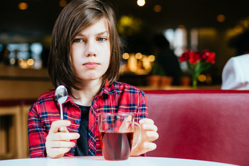 Close up portrait of teenager boy drinking tea sitting on red couch having breakfast in cafe interior.