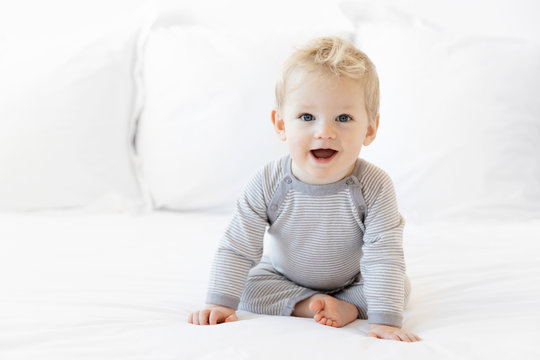 Cute blonde baby boy sitting on white bed