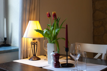 Dining wooden table with white tablecloth, tulips bouquet and glasses