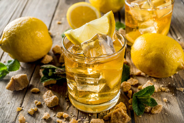 Lemonade or iced summer tea, with fresh lemon slices, sugar and mint leaf, rustic wooden table, copy space