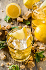 Lemonade or iced summer tea, with fresh lemon slices, sugar and mint leaf, rustic wooden table, copy space