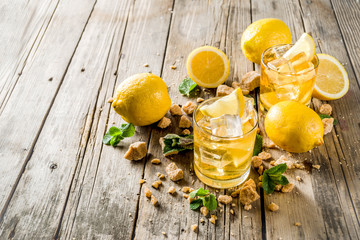 Lemonade or iced summer tea, with fresh lemon slices, sugar and mint leaf, rustic wooden table, copy space