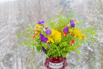 Fototapeta na wymiar A beautiful vase of spring flowers stands on a window in a snowstorm