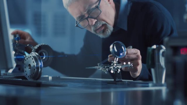 Close-up Portrait of Focused Middle Aged Engineer in Glasses Working with High Precision Laser Equipment, Using Lenses and Testing Optics for Accuracy Required Electronics