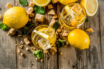 Lemonade or iced summer tea, with fresh lemon slices, sugar and mint leaf, rustic wooden table, copy space