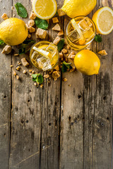 Lemonade or iced summer tea, with fresh lemon slices, sugar and mint leaf, rustic wooden table, copy space