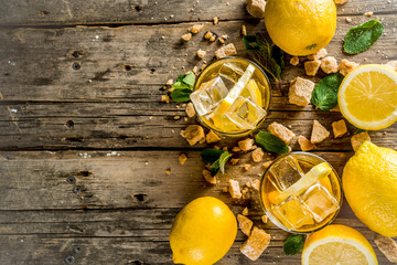 Lemonade or iced summer tea, with fresh lemon slices, sugar and mint leaf, rustic wooden table, copy space