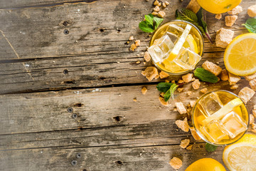 Lemonade or iced summer tea, with fresh lemon slices, sugar and mint leaf, rustic wooden table, copy space
