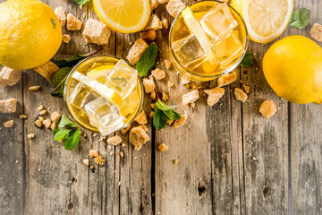 Lemonade or iced summer tea, with fresh lemon slices, sugar and mint leaf, rustic wooden table, copy space