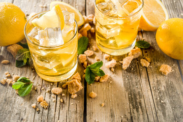 Lemonade or iced summer tea, with fresh lemon slices, sugar and mint leaf, rustic wooden table, copy space