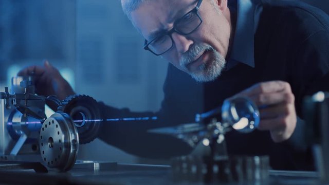 Close-up Portrait of Focused Middle Aged Engineer in Glasses Working with High Precision Laser Equipment, Using Lenses and Testing Optics for Accuracy Required Electronics