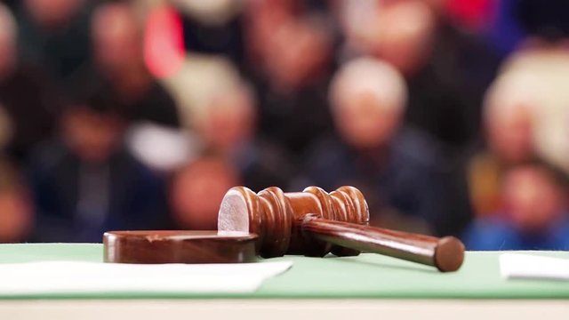 auctioneer or judge gavel mallet in foreground focused with public or jury in background unfocused , HD video footage