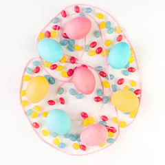 Colorful Easter egg concept. Easter eggs and candies with pink satin ribbon on isolated white background. Flat lay.