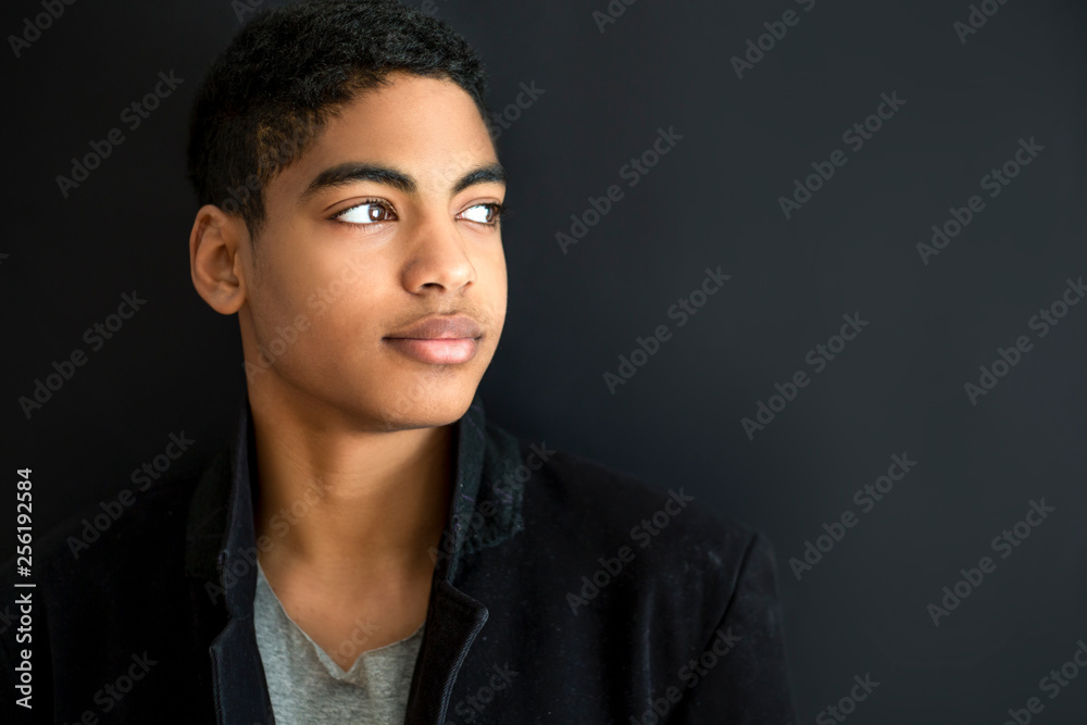 Wall mural Fashion portrait of a beautiful boy on a black background. Portrait of a young African American man. Attractive teenager. 