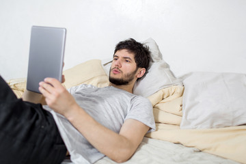Young man is in bed with a tablet in his hands. White background