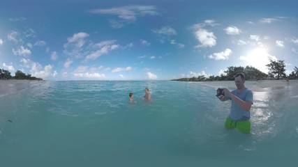 MAURITIUS ISLAND - JUNE 08, 2016: 360 VR video. Mauritius beach with resort area and happy mother with son bathing in the ocean and having fun, father taking photos and video on mobile. Family (with