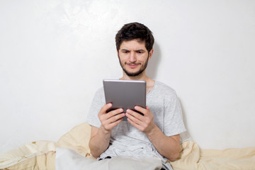 Young man is in bed with a tablet in his hands. White background