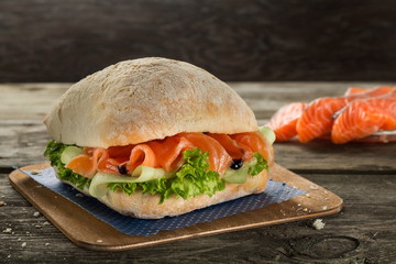 Ciabatta burger with salmon, cucumber and salad served on the wooden table