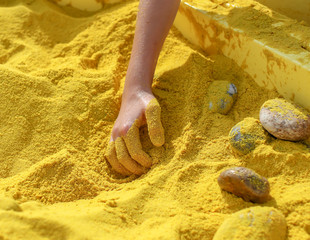 The child plays with his hands in the yellow sand