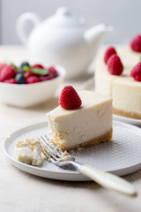 Piece of birthday cheese cake with raspberry at gray plate on white background