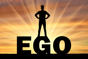 Silhouette of a man with a crown on his head standing on the word ego against the backdrop of a...