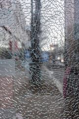 Close-up of a broken and shattered glass pane or window, blurred city view in the background.